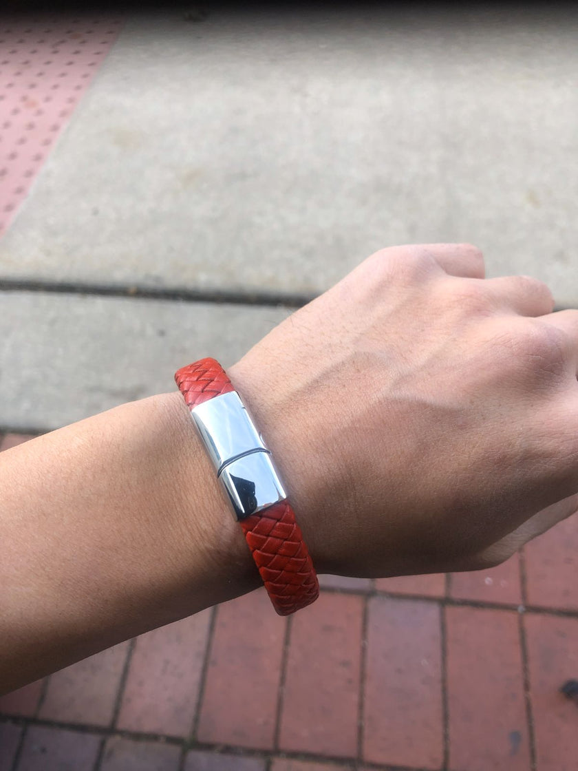 Red bracelet with a silver clasp on a wrist, against a pavement background