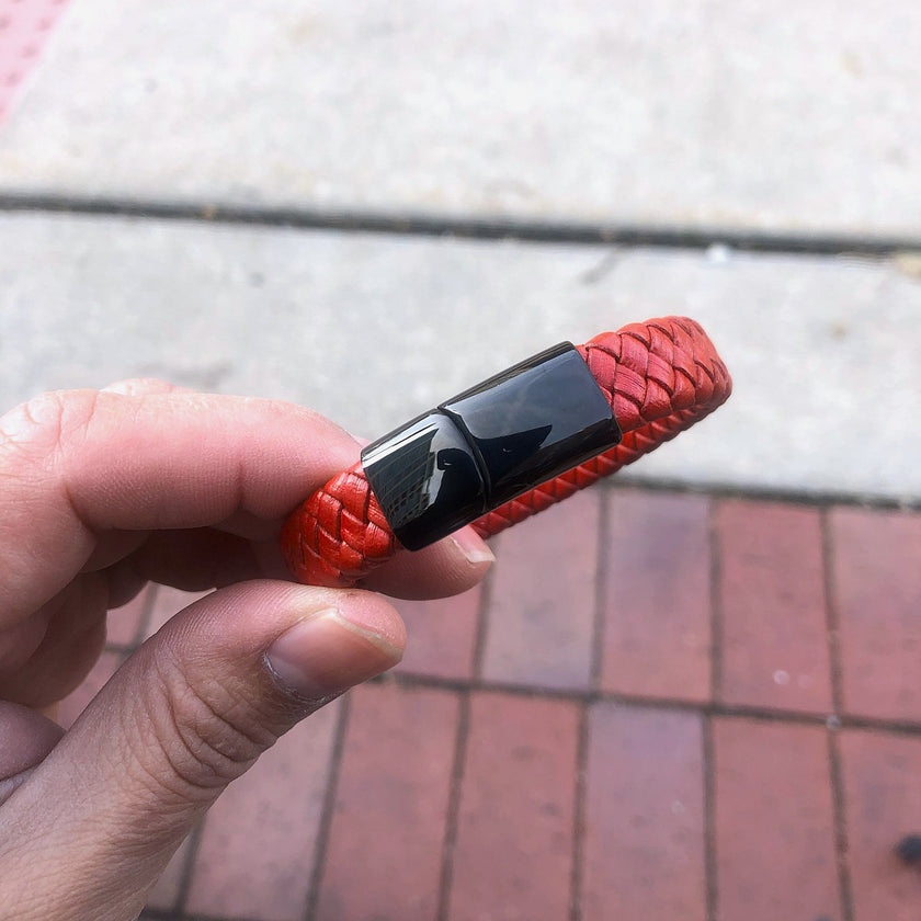 Red braided bracelet with a black clasp held by a hand on a pavement background